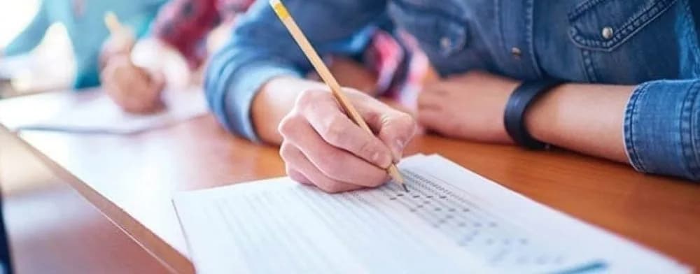 A student filling in a multiple-choice answer sheet with a pencil at an exam desk.